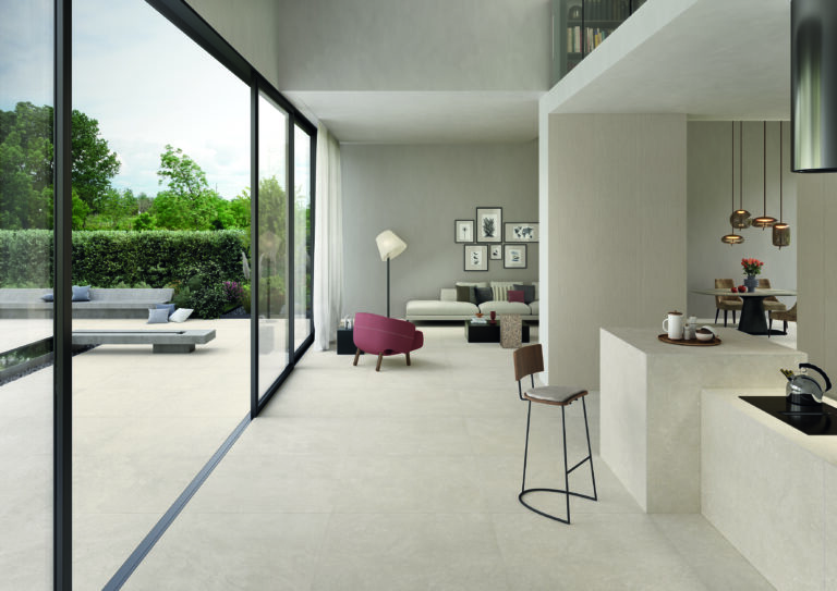 Binnen-buitenconcepten met doorlopende betonlook tegelvloer, modern open interieur met glazen schuifwand naar tuin, naadloze overgang tussen woonkamer en terras, wit keukeneiland met hangende koperen lampen